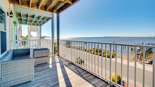 Une terrasse en bois, meublée de meubles en osier, dotée d’une rambarde et offrant une vue sur la plage et l’océan.