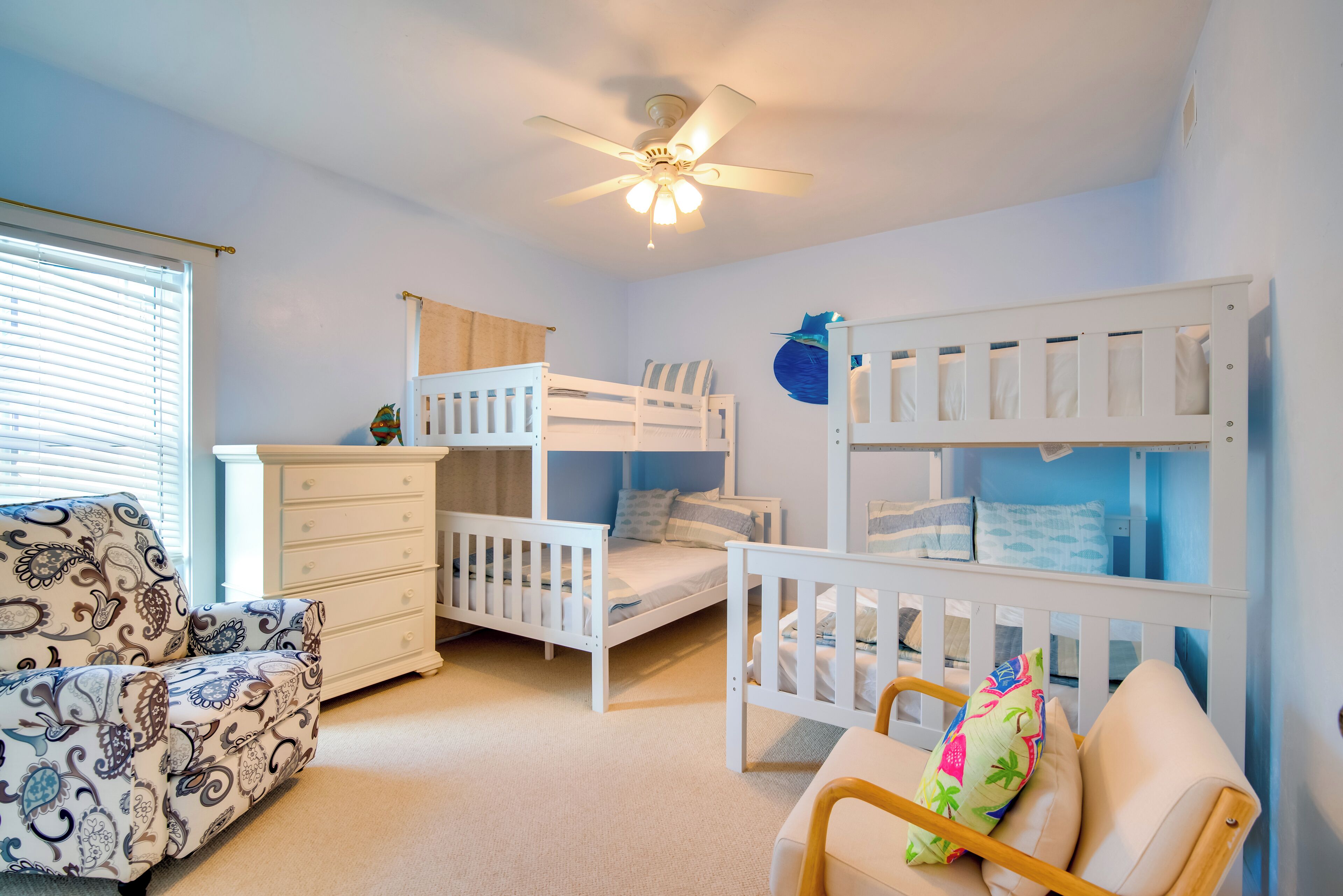 Une chambre d’enfant avec des lits superposés, une commode, une chaise et un ventilateur de plafond.