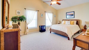 Une chambre avec un grand lit, un ventilateur de plafond et une fenêtre avec des rideaux.