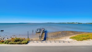 Une route côtière avec une jetée qui s’avance dans des eaux calmes, un ciel dégagé et, au loin, une terre ferme couverte de végétation.