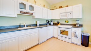 Une cuisine avec des armoires blanches, un four à micro-ondes, une cuisinière et une poubelle.