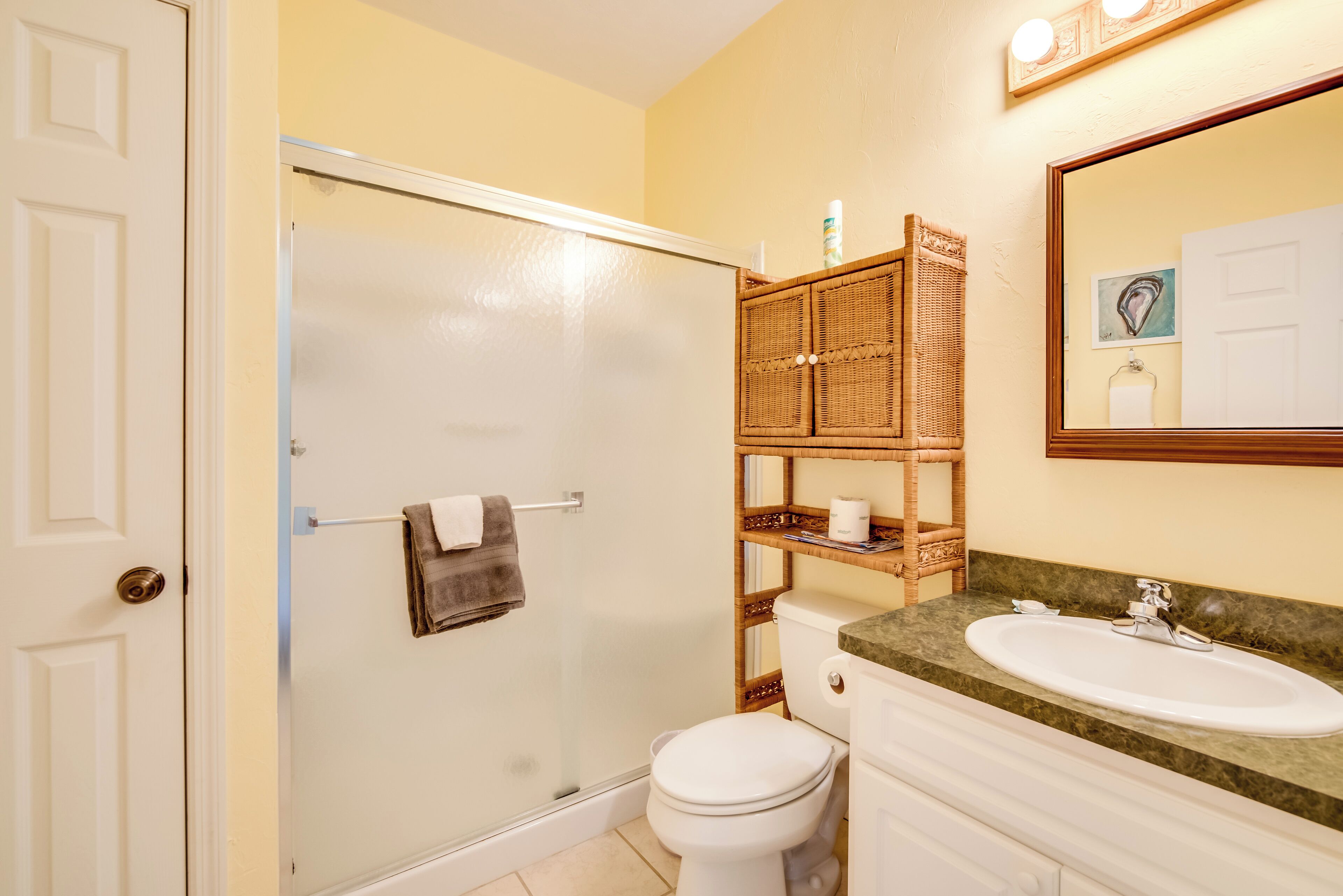 A bathroom with a glass-enclosed shower, a toilet, a sink, and a wicker shelf with toiletries.