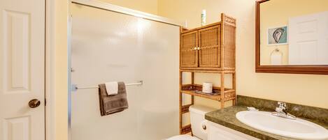 A bathroom with a glass-enclosed shower, a toilet, a sink, and a wicker shelf with toiletries.