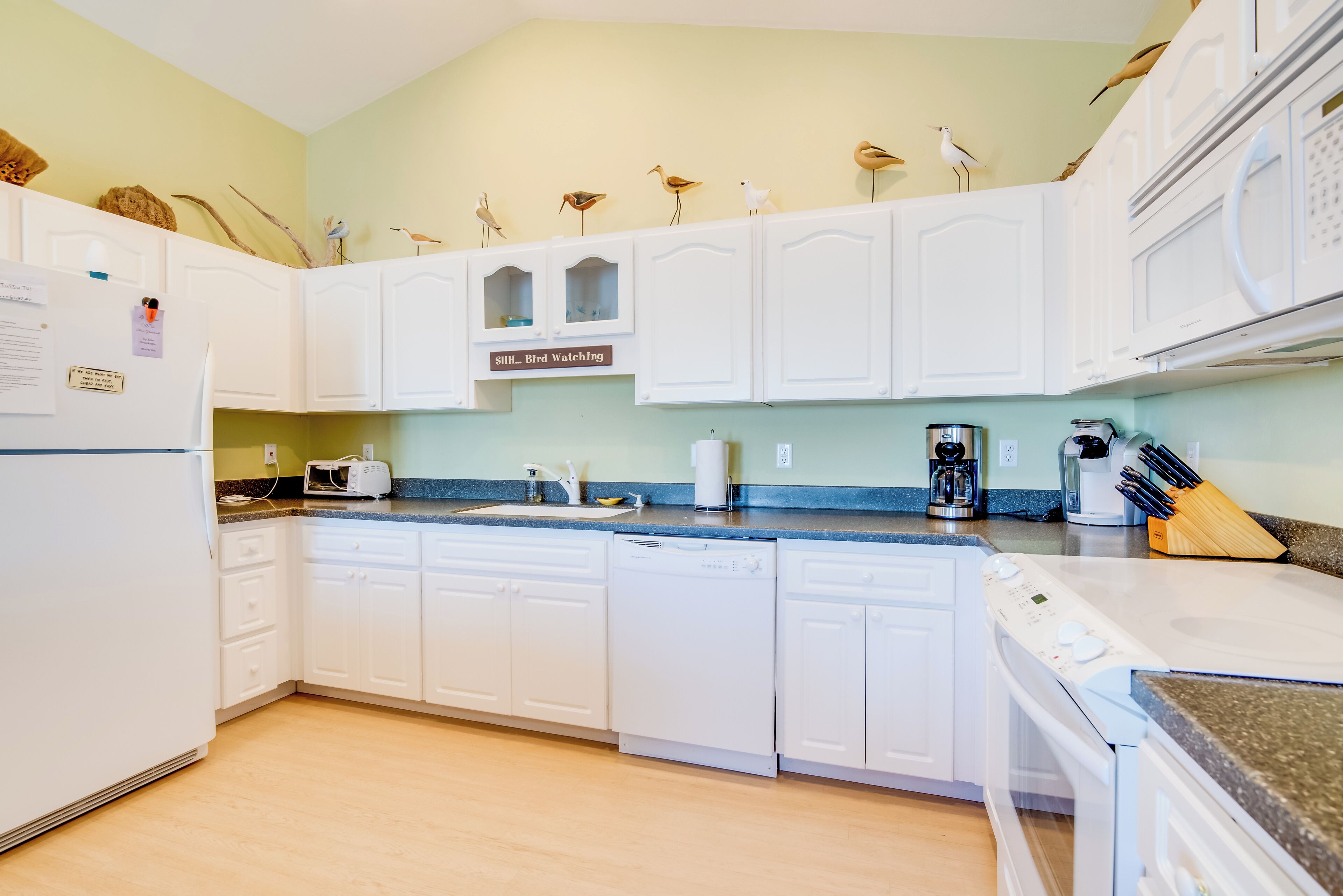 A kitchen with white cabinets, a dishwasher, a stove, a microwave, and a coffee maker. There are decorative bird figures on the cabinets.