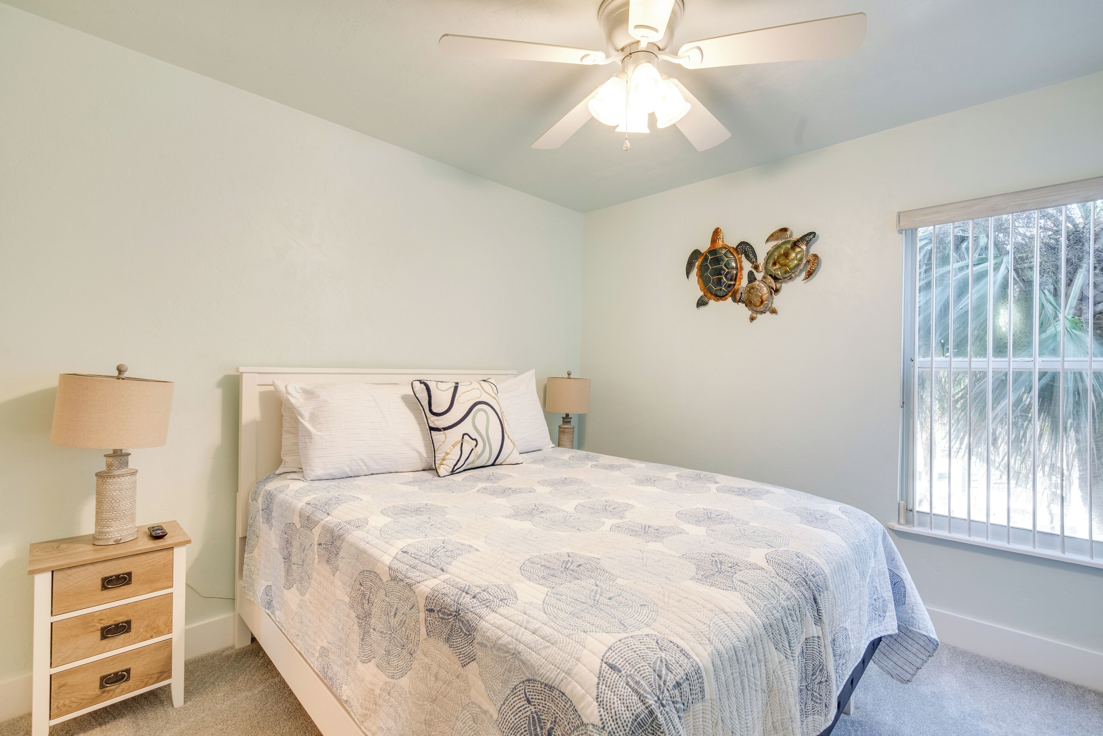 Une chambre à coucher comprenant un lit, deux lampes de chevet, un ventilateur de plafond, une fenêtre avec vue et un élément décoratif mural.