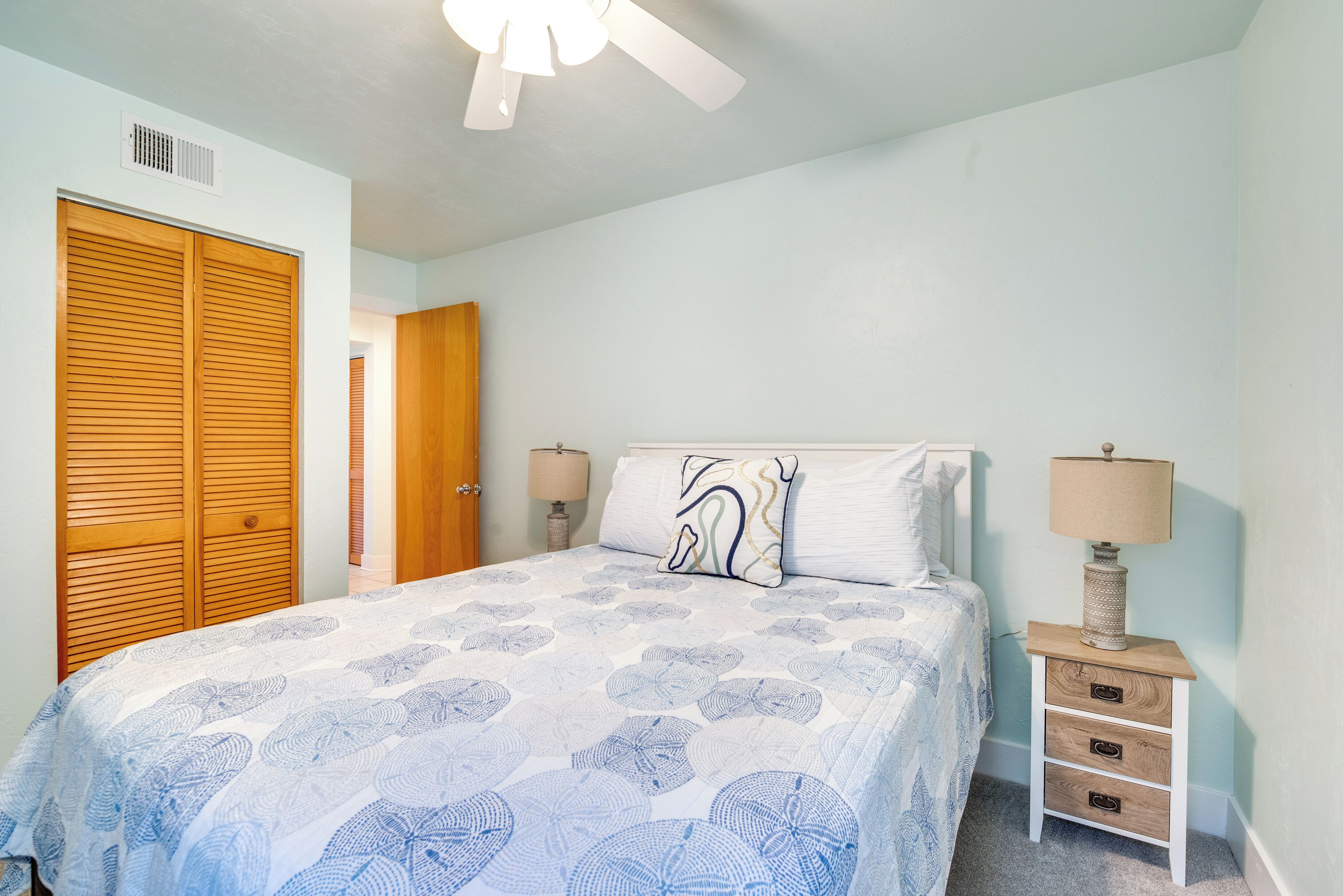 A bedroom with a bed, a nightstand, a lamp, a ceiling fan, and a wooden wardrobe.