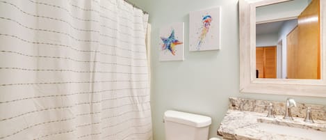 A bathroom with a striped shower curtain, a toilet, a sink with a marble countertop, and two wall-mounted light fixtures.