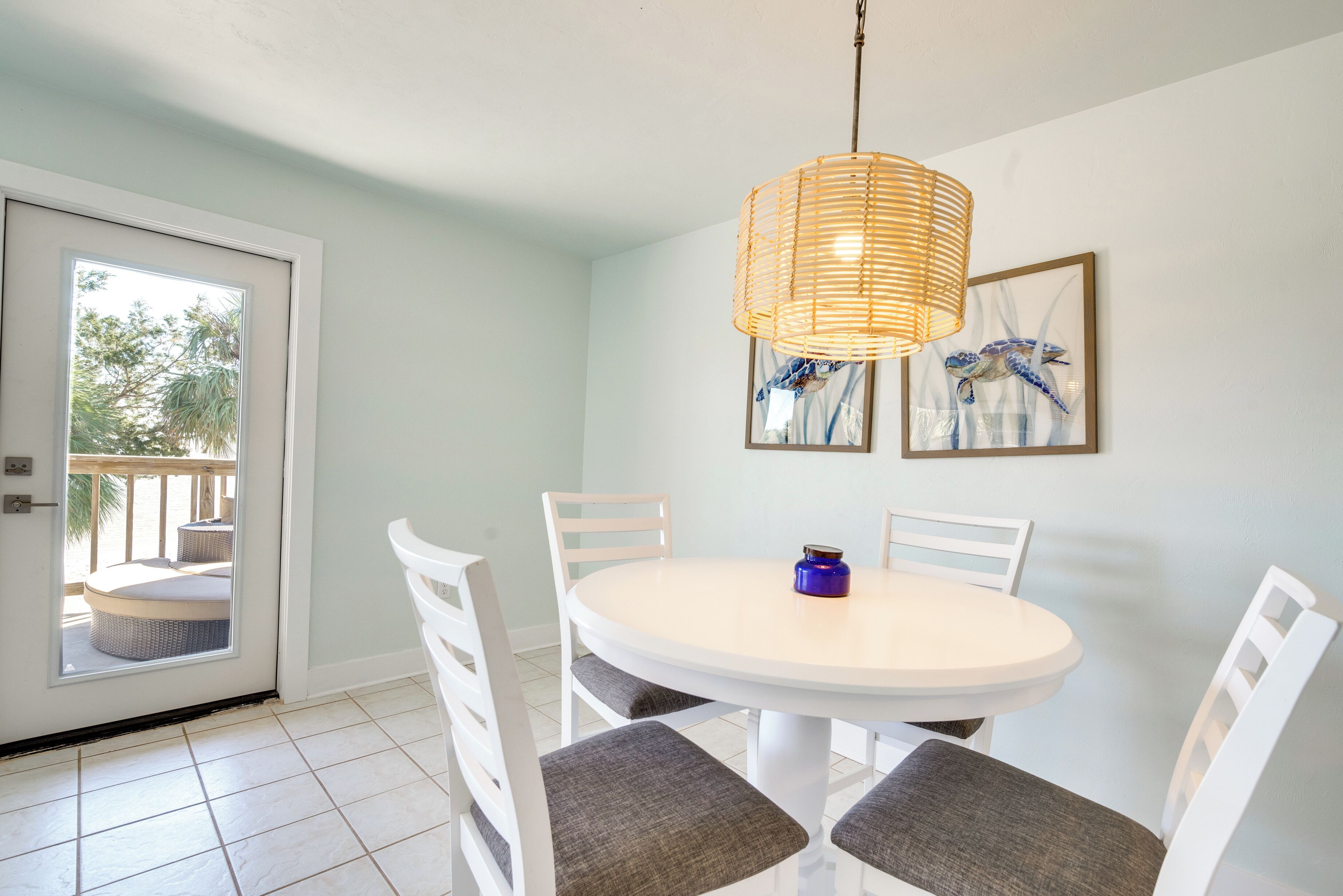 A dining area with a round table, white chairs, a wicker pendant light, and a door leading to an outdoor seating area.