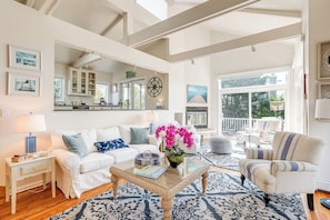 Un salon spacieux avec une grande fenêtre, une cuisine à l’arrière-plan et un balcon aménagé avec du mobilier d’extérieur.