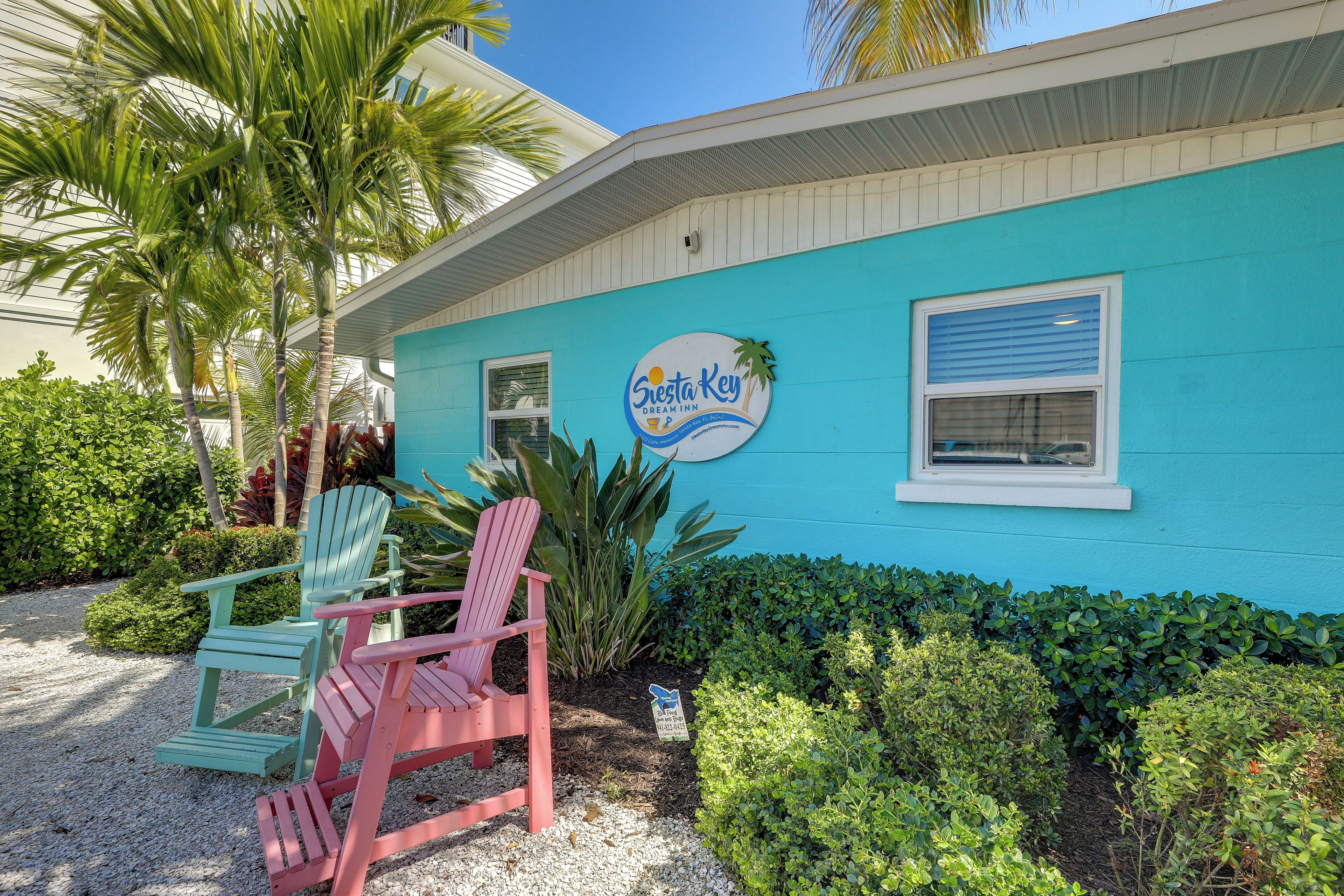 A blue building with a sign that reads "Siesta Key Dream Inn" and two Adirondack chairs in front.