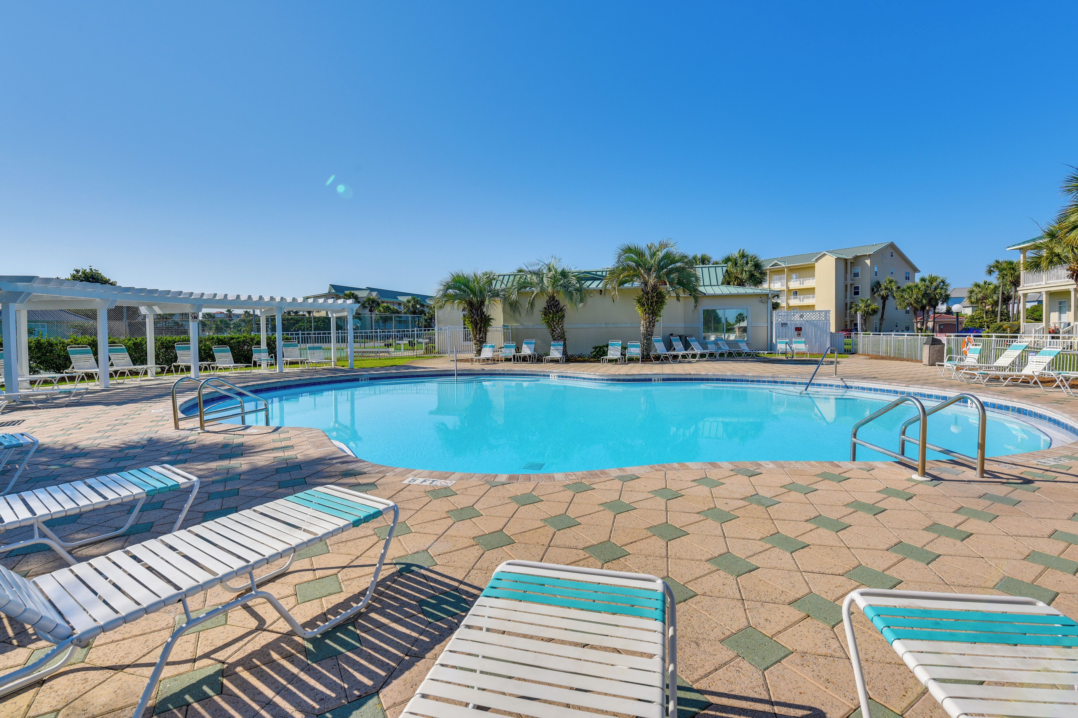 Ein Swimmingpool mit Liegestühlen und einer überdachten Liegefläche, umgeben von Gebäuden und Palmen.