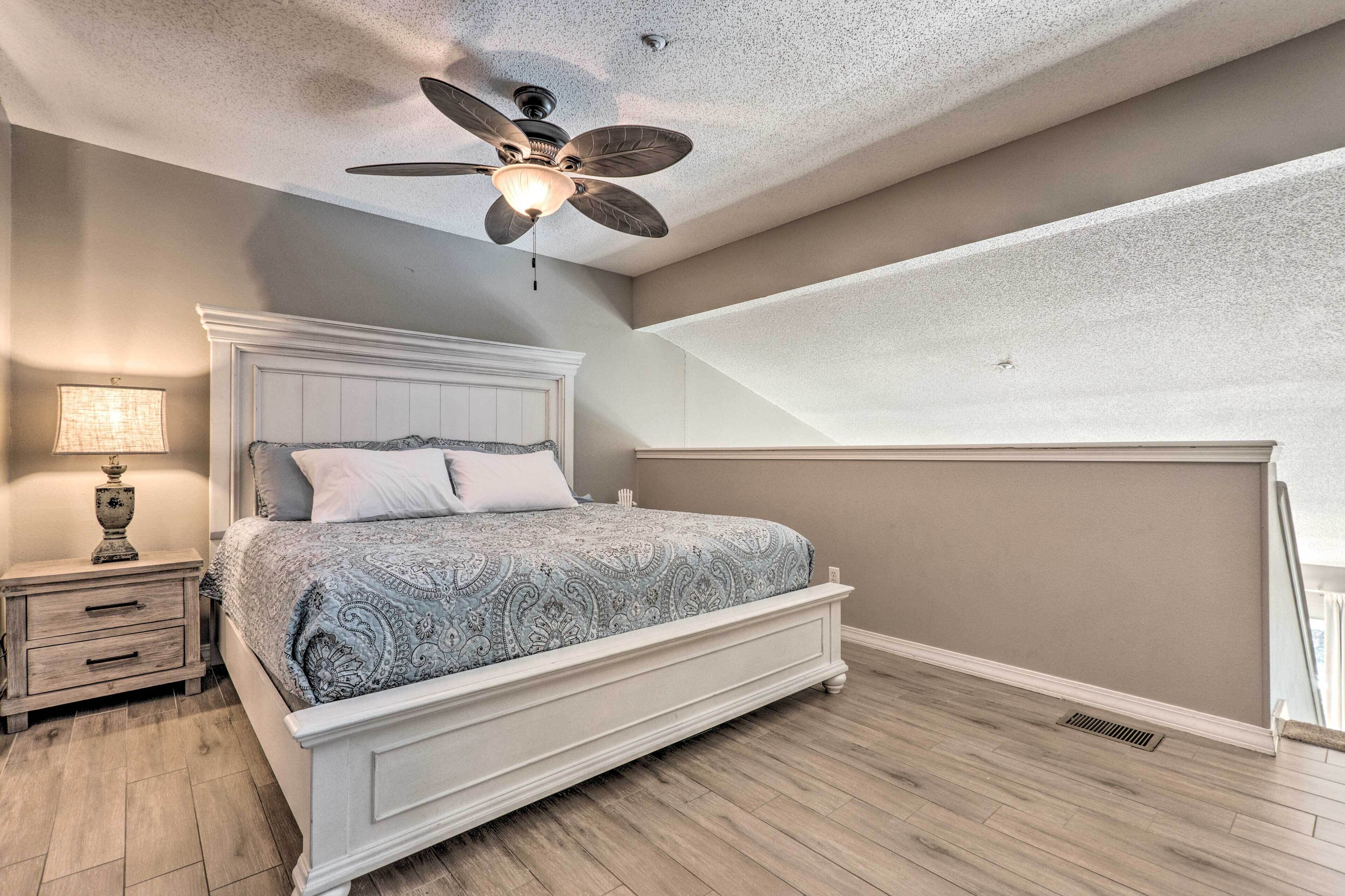 A bedroom with a bed, nightstand, lamp, ceiling fan, and sloped ceiling.