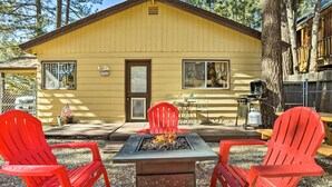 Une cabane en bois jaune avec un foyer au centre, entourée de chaises Adirondack rouges.
