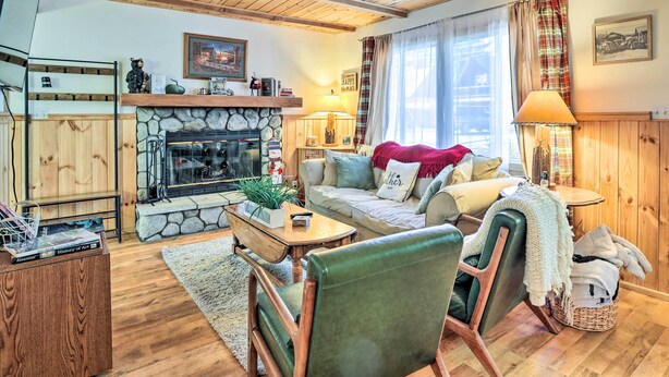 Un salon chaleureux avec une cheminée en pierre, des poutres en bois, un canapé et un fauteuil en cuir vert.