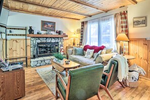 A cozy living room with a stone fireplace, wooden beams, a sofa, and a green leather chair. - Charming Big Bear Cabin w/ Gas Grill (Big Bear City)