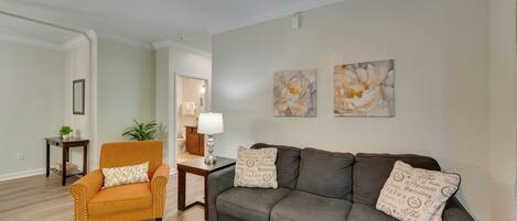 A living room with a sofa, armchair, and coffee table. There are two wall-mounted paintings and a ceiling fan.