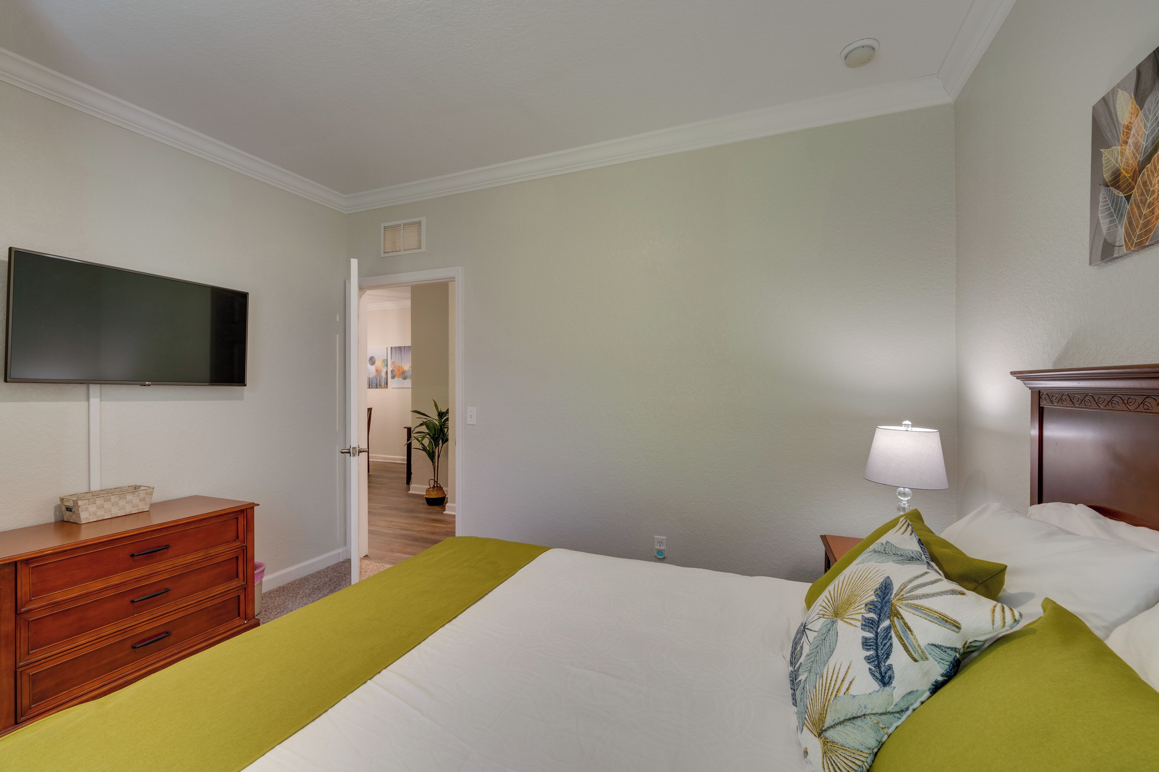 Quarto de hotel com cama, televisão, penteadeira e mesa de cabeceira com abajur.