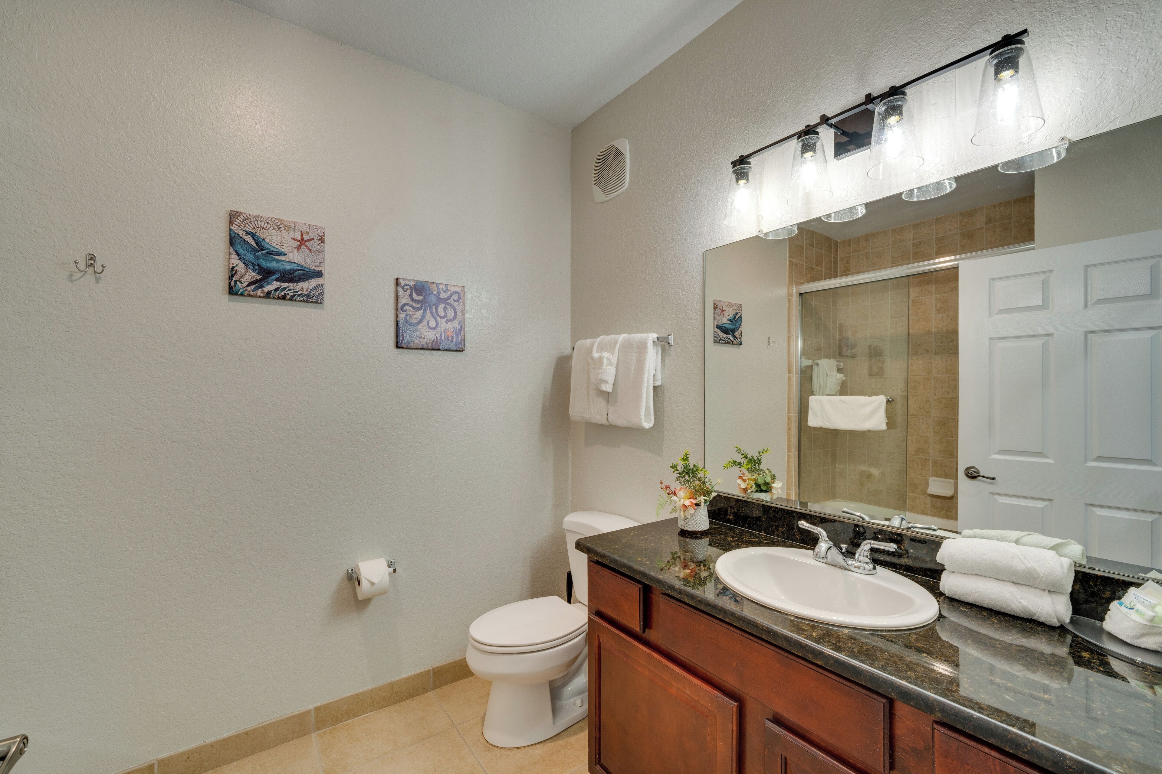 A modern bathroom with a white toilet, a sink with a mirror above it, and artwork on the walls.