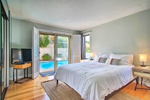 A bedroom with a large bed, a TV, and a sliding glass door leading to a pool. - 2 Mi to Beach: Retreat w/ Pool & Grill in Mashpee! (Mashpee)