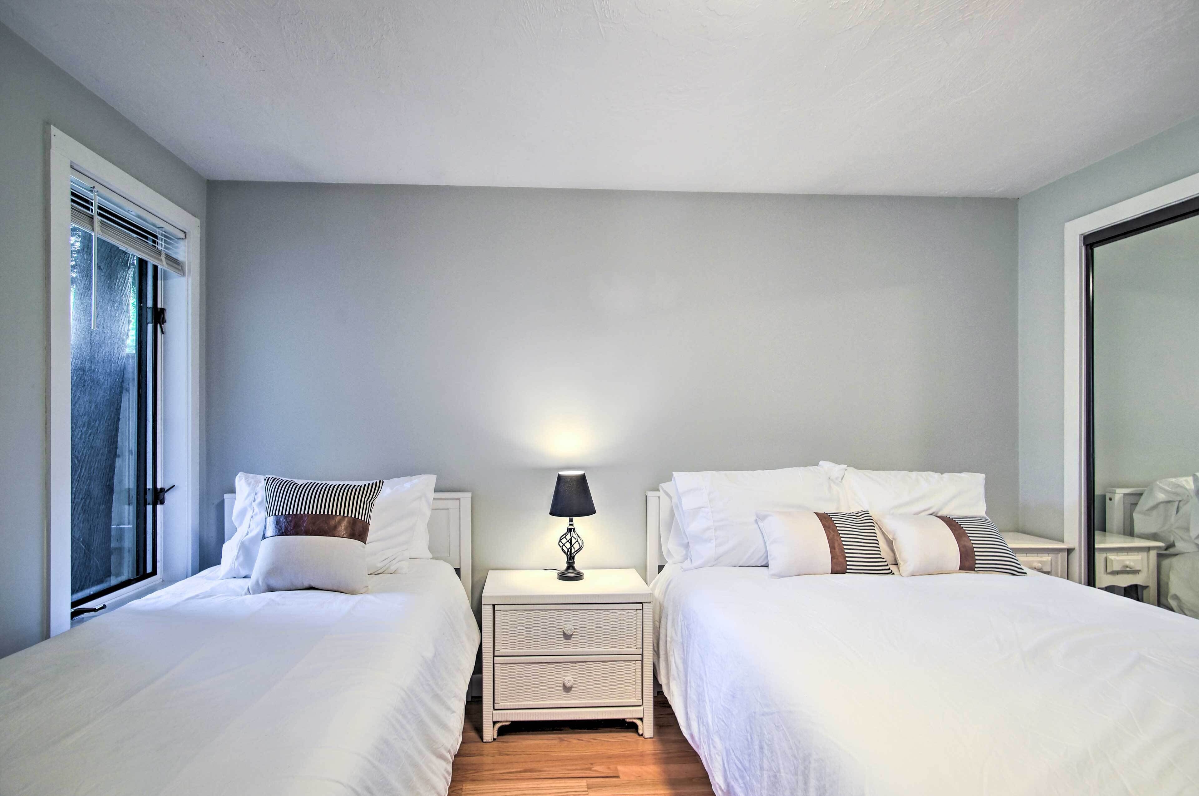 A hotel room with two beds, a nightstand with a lamp, and a window with blinds.
