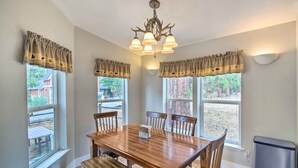 Un coin repas avec une table et des chaises en bois, un lustre et de grandes fenêtres ornées de rideaux.
