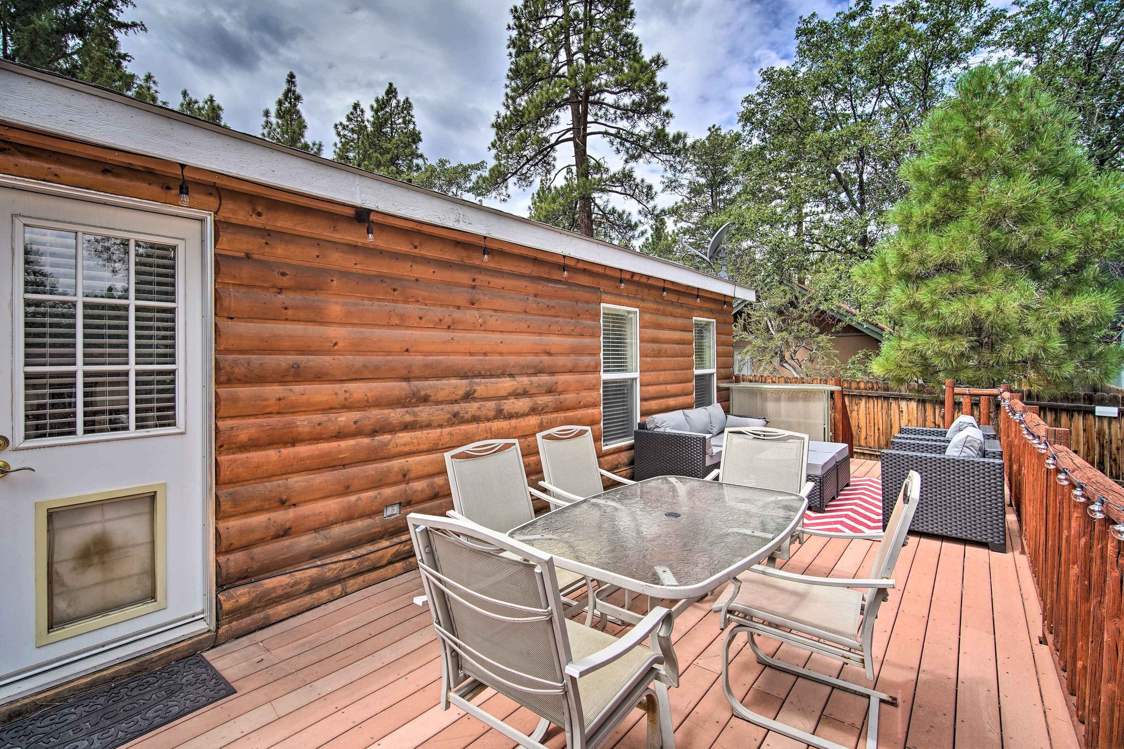 A wooden cabin with a deck, outdoor seating, and a large window.