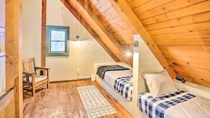 Un dormitorio acogedor en el ático con vigas de madera, una ventana, una cama, una silla y una alfombra estampada.