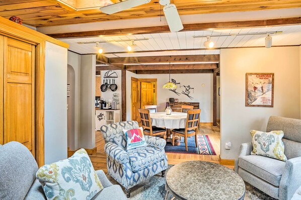 A cozy living room with a patterned armchair, a round coffee table, and a dining area with a table and chairs.