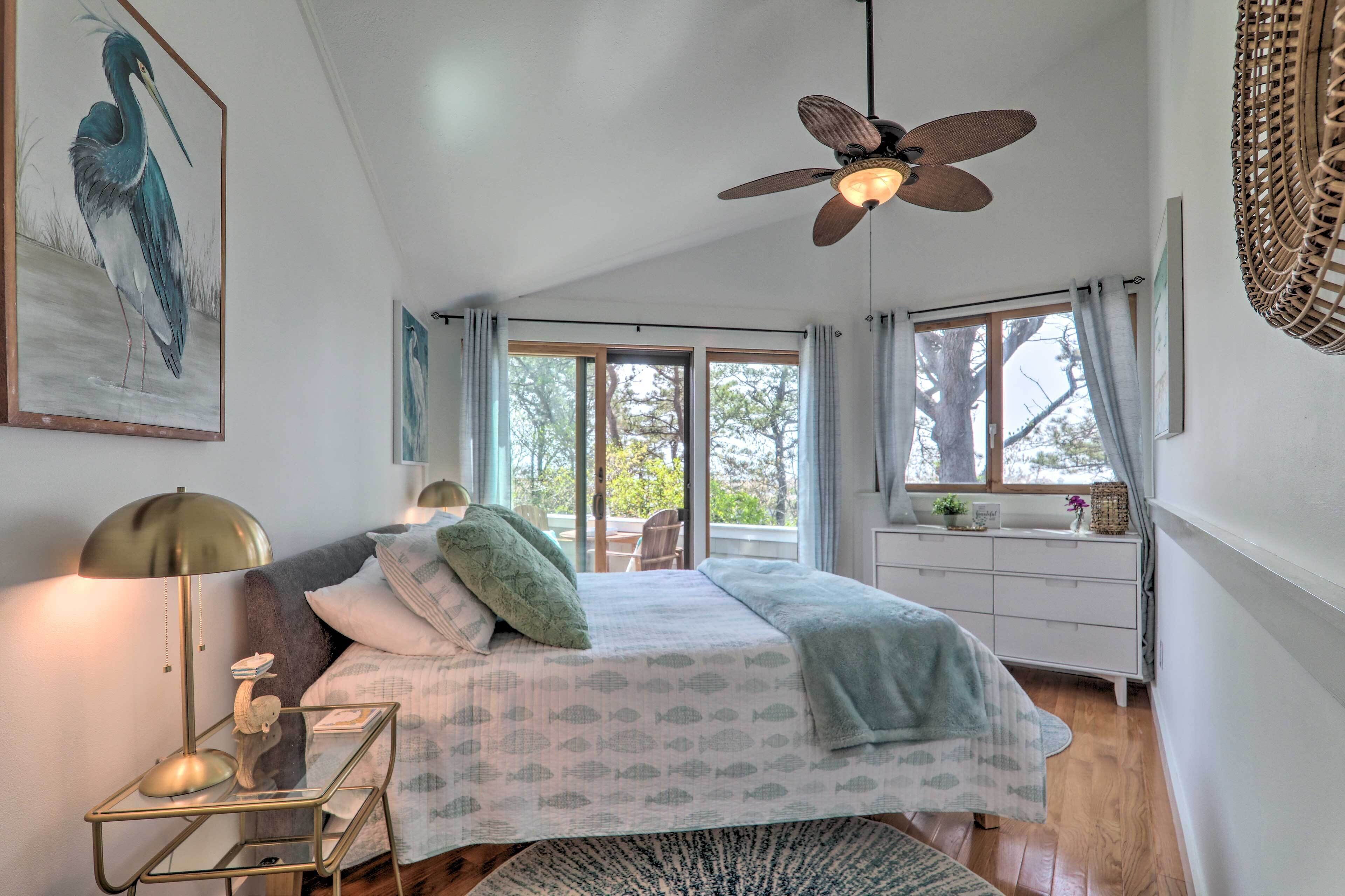 A bedroom with a bed, a standing lamp, a ceiling fan, and a window with curtains.