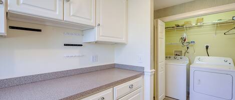 A laundry area with two washing machines, a dryer, and a countertop with cabinets.