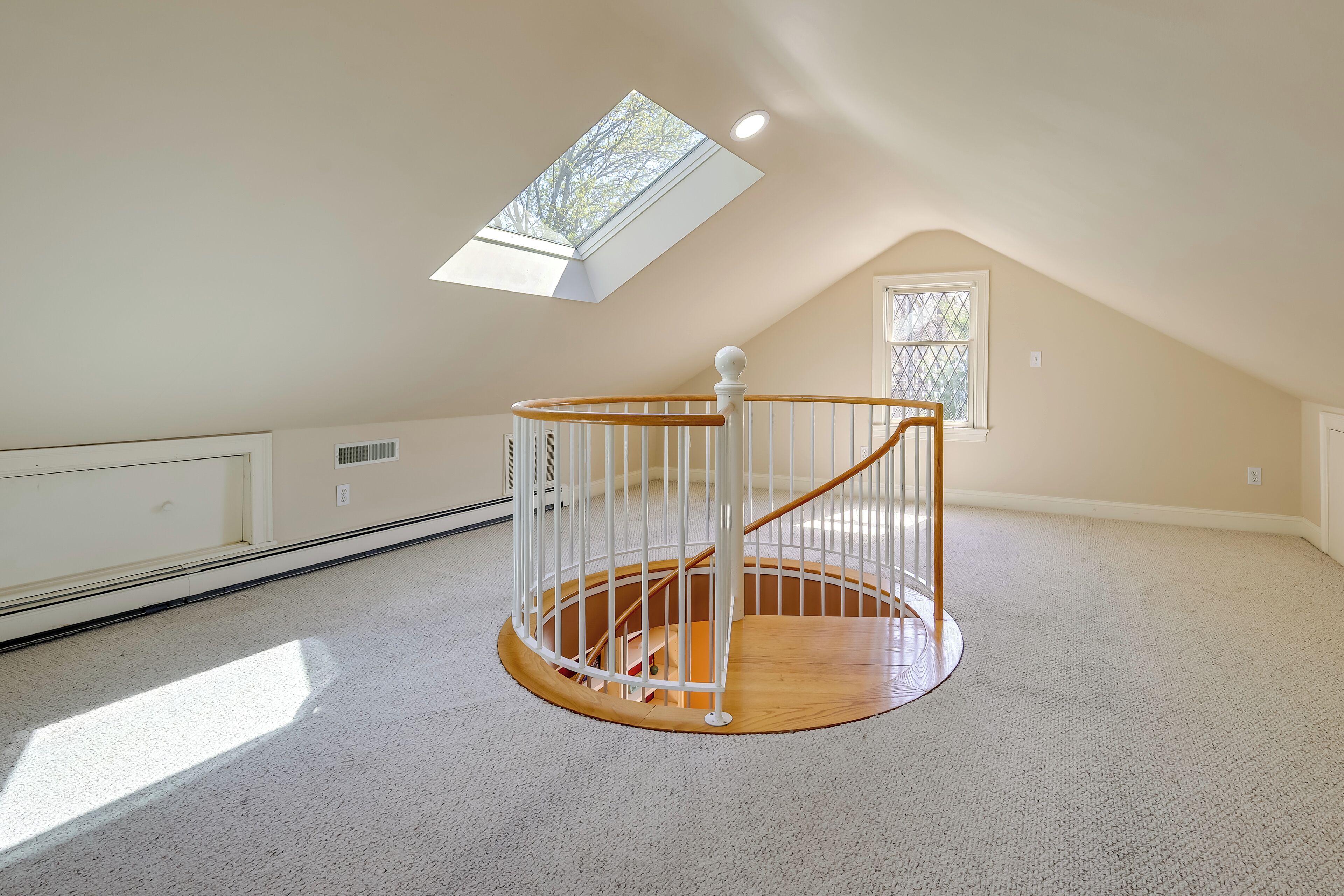 A spacious attic room with a skylight, a wooden spiral staircase, and a large window.