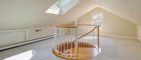A spacious attic room with a skylight, a wooden spiral staircase, and a large window.