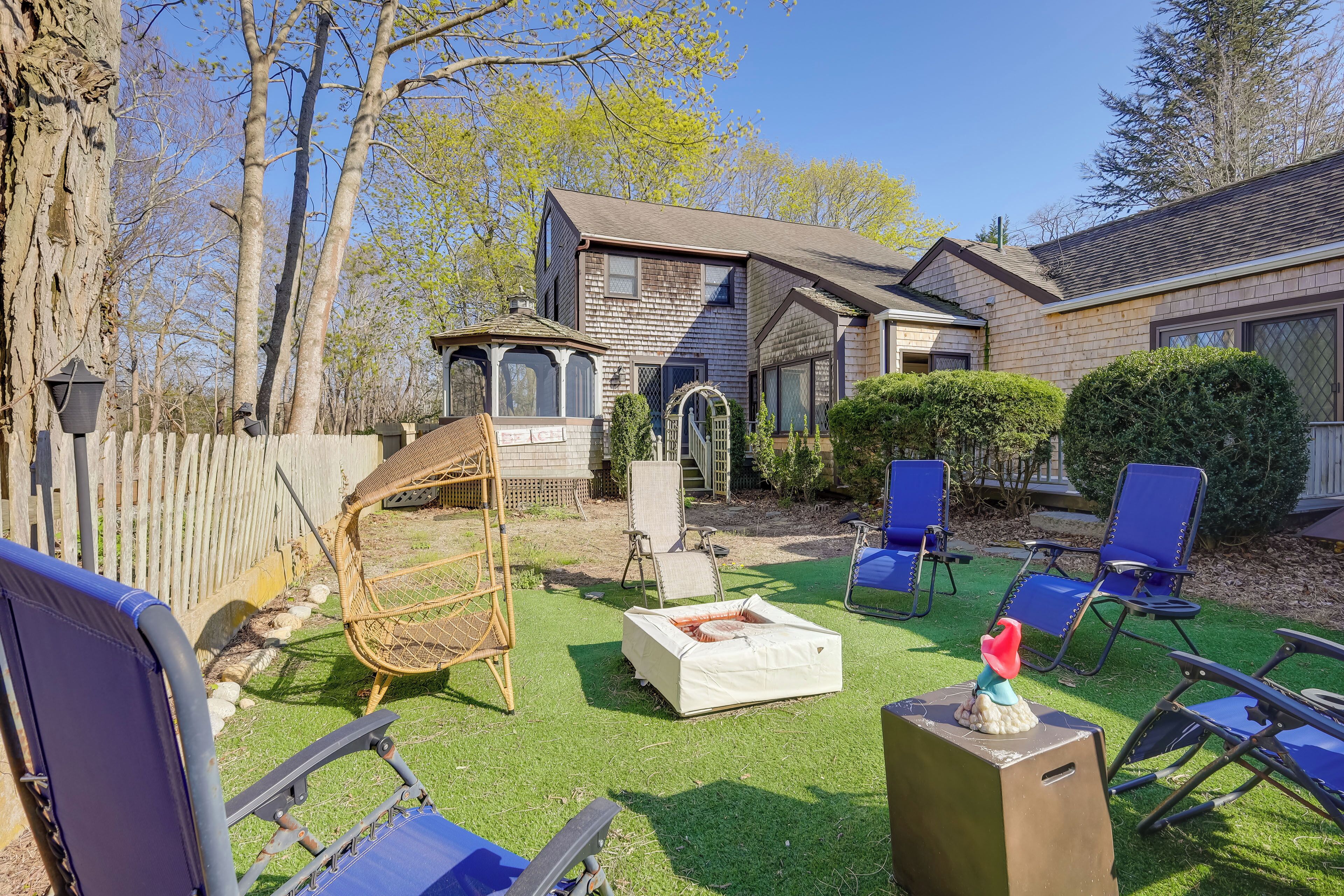 Un jardin avec une terrasse en bois, un kiosque et une pelouse agrémentée de chaises de jardin bleues.