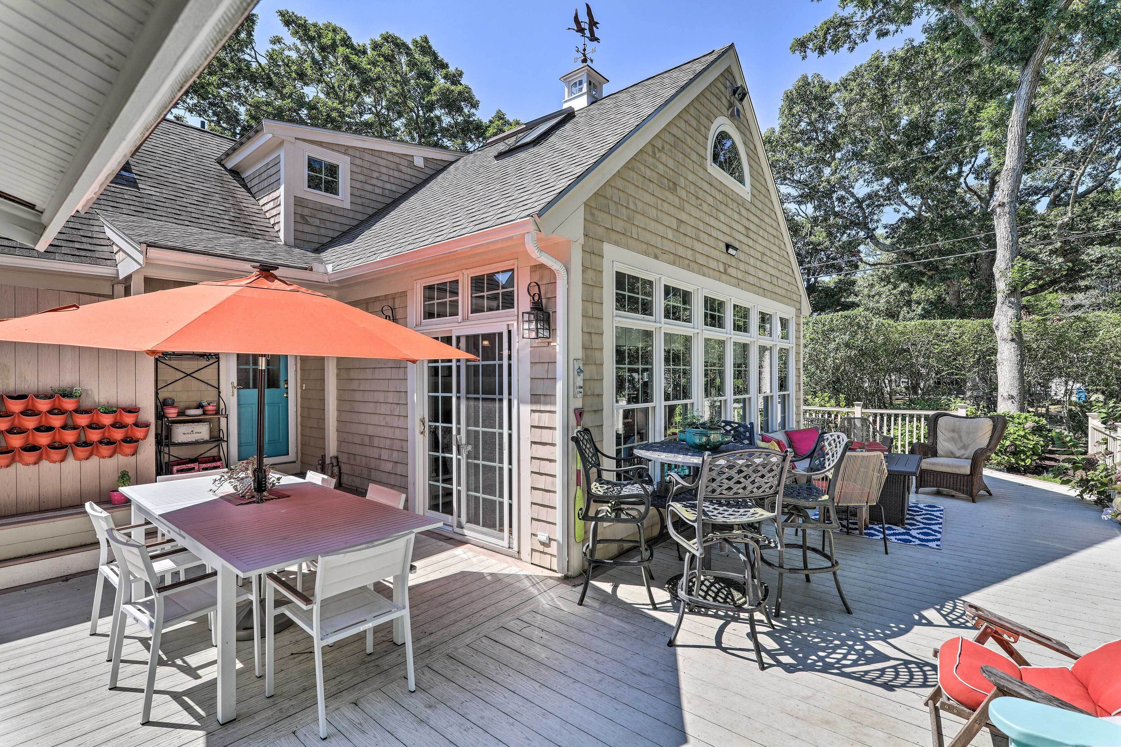 A covered patio with a table and chairs, surrounded by potted plants and a wooden deck.