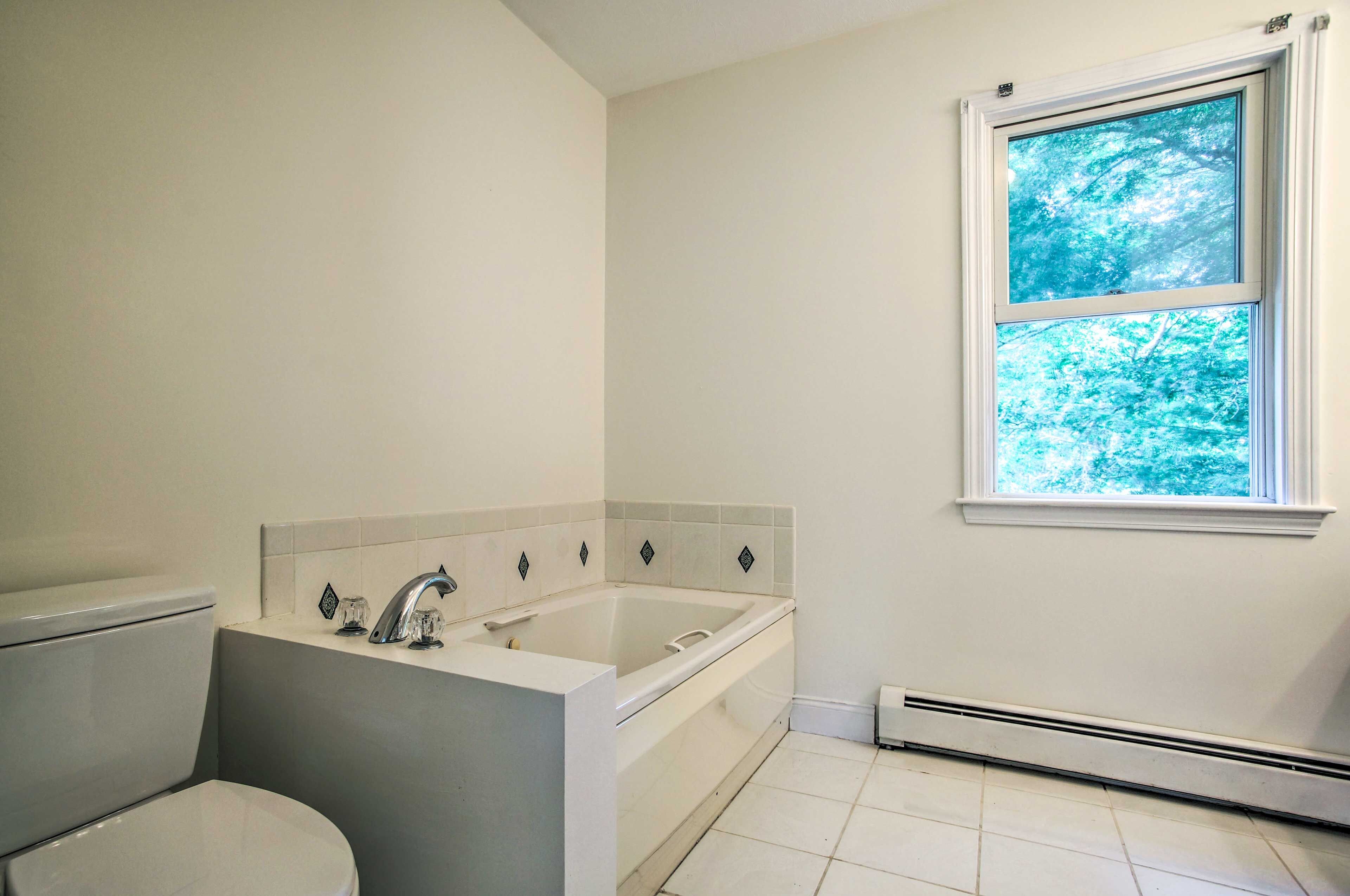 Ein Badezimmer mit Badewanne, Toilette und einem Fenster mit Blick auf Bäume.