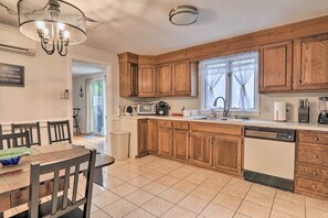 A kitchen with wooden cabinets, a dishwasher, and a dining area with chairs and a table. - West Yarmouth Home w/ Deck < 2 Mi to Beach! (West Yarmouth)