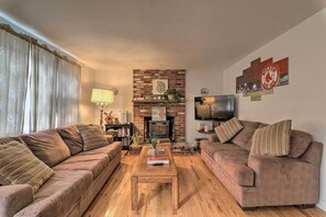 A living room with two sofas, a coffee table, a fireplace, and a wall-mounted TV. - West Yarmouth Home w/ Deck < 2 Mi to Beach! (West Yarmouth)