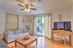 A living room with a sofa, a coffee table with seashells, a TV on a wooden stand, and a ceiling fan. - West Yarmouth Home w/ Deck < 2 Mi to Beach! (West Yarmouth)