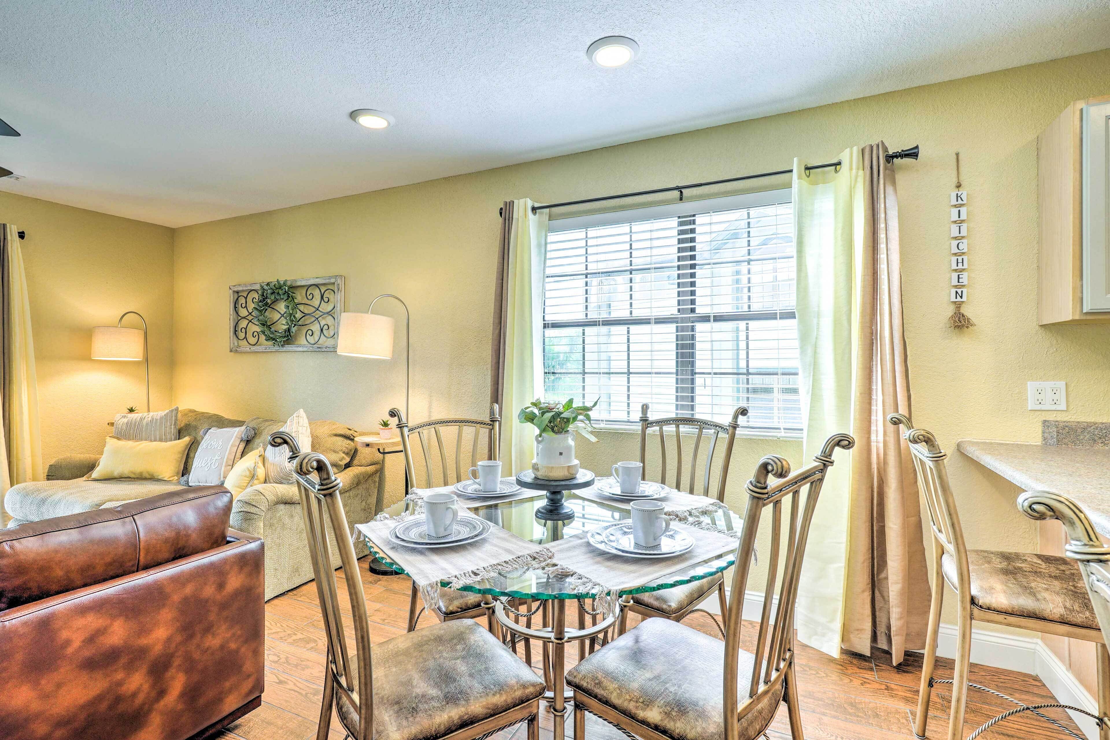 A dining area with a glass table, metal chairs, and a sofa in the background.