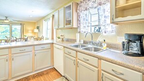 A kitchen with white cabinets, a granite countertop, a coffee maker, and a window with a curtain.