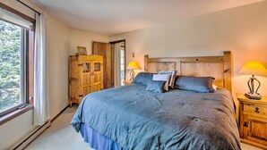 A bedroom with a large bed, wooden headboard, two bedside lamps, and a window with curtains. - New Mexico Condo w/ Fireplace & Mountain View (Angel Fire)