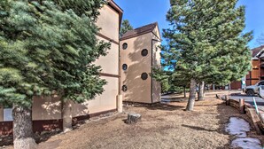 A building with a beige exterior and multiple windows, surrounded by trees and a gravel path. - New Mexico Condo w/ Fireplace & Mountain View (Angel Fire)