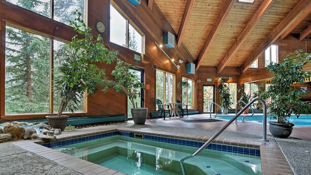 An indoor pool with a view of trees, wooden beams, and a seating area with chairs and tables.