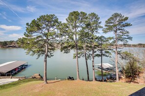 A lakeside view with a dock, a covered seating area, and tall pine trees.