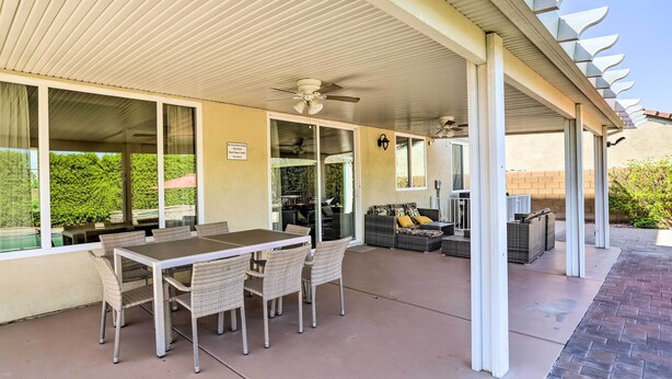 A covered patio area with a dining table and chairs, a ceiling fan, and a seating area with cushions. - Welcoming Coachella Home w/ Heated Salt Pool! (Coachella)