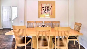 A dining area with a wooden table and chairs, a wall-mounted artwork, and a door leading to another room. - Welcoming Coachella Home w/ Heated Salt Pool! (Coachella)