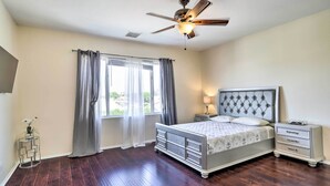 A bedroom with a bed, nightstands, a ceiling fan, and a window with curtains. - Welcoming Coachella Home w/ Heated Salt Pool! (Coachella)