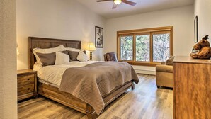 A bedroom with a wooden bed, a nightstand, a lamp, a chair, a desk, and a window with a view of trees. - Forest-view Gem 2 Mi to Diamond Peak Ski Resort! (Incline Village)