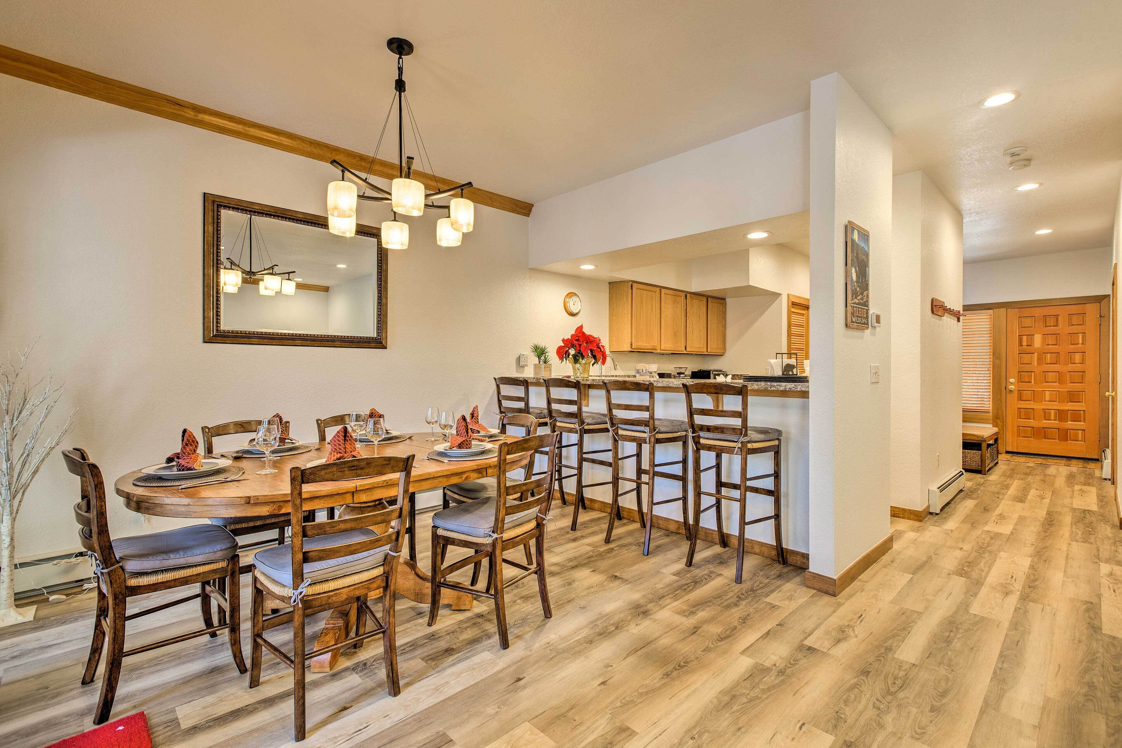 A dining area with a wooden table and chairs, a hanging light fixture, and wooden cabinets in the background.