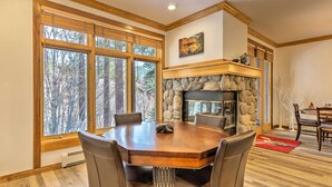 A dining area with a large wooden table, leather chairs, a stone fireplace, and a view of trees through large windows. - Forest-view Gem 2 Mi to Diamond Peak Ski Resort! (Incline Village)